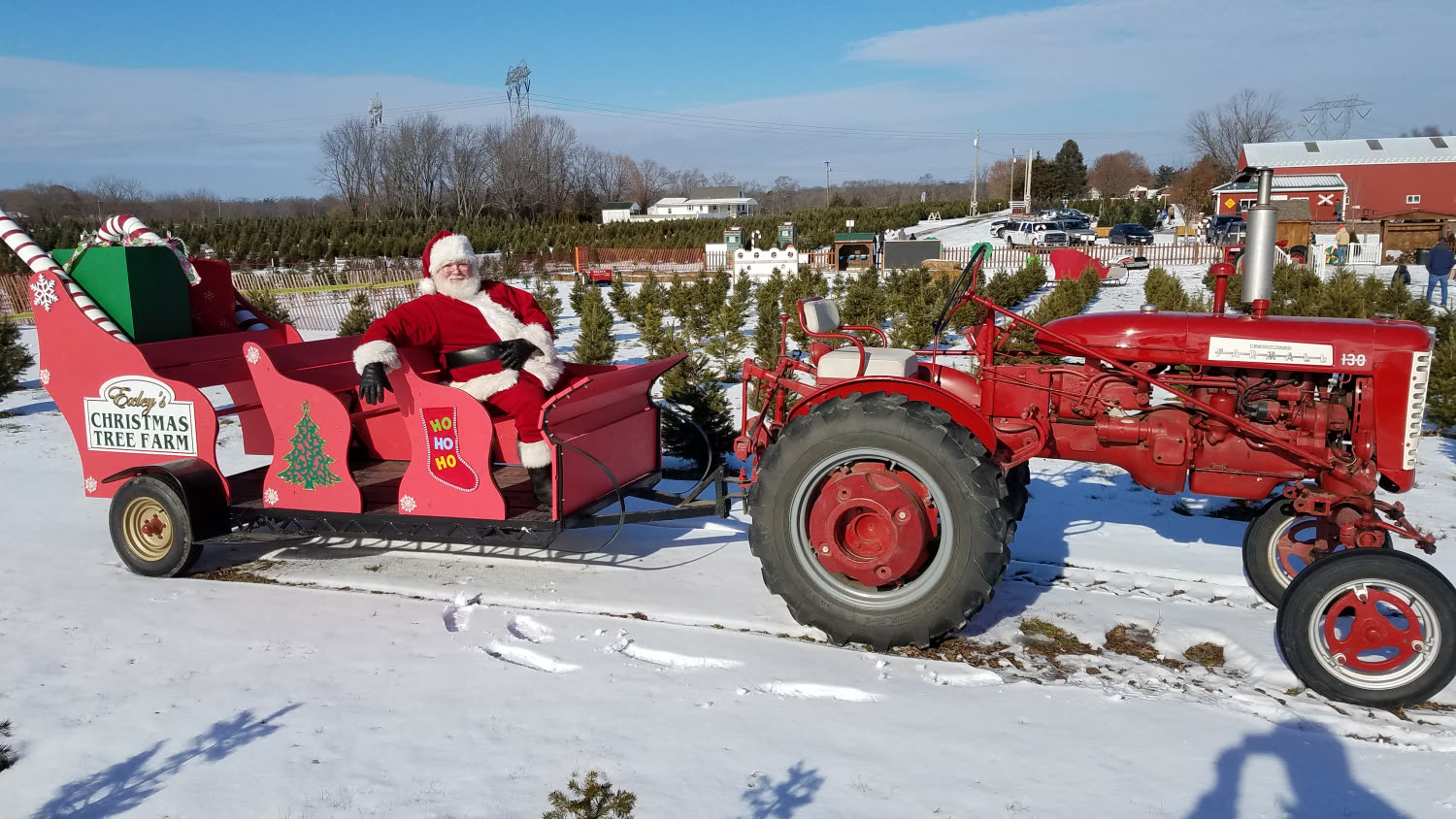 Santa riding in the sleigh pulled by a red antique tractor through the snowy tree field